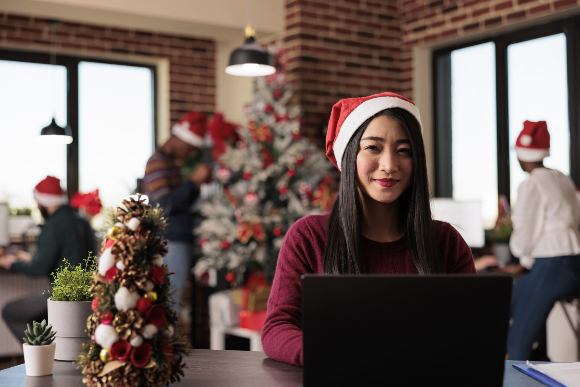 Portrait of business woman working in christmas season in startup office decorated with festive xmas ornaments and lights. Asian company worker using laptop during seasonal celebration