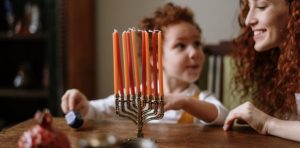 Mother and child celebrating Hannukah, they are looking at a menorah candle holder on the table
