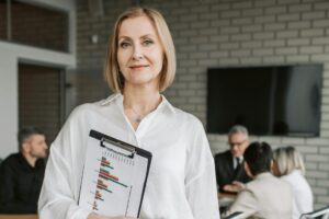 Person in white blouse looking at the camera. They are holding a clipboard.
