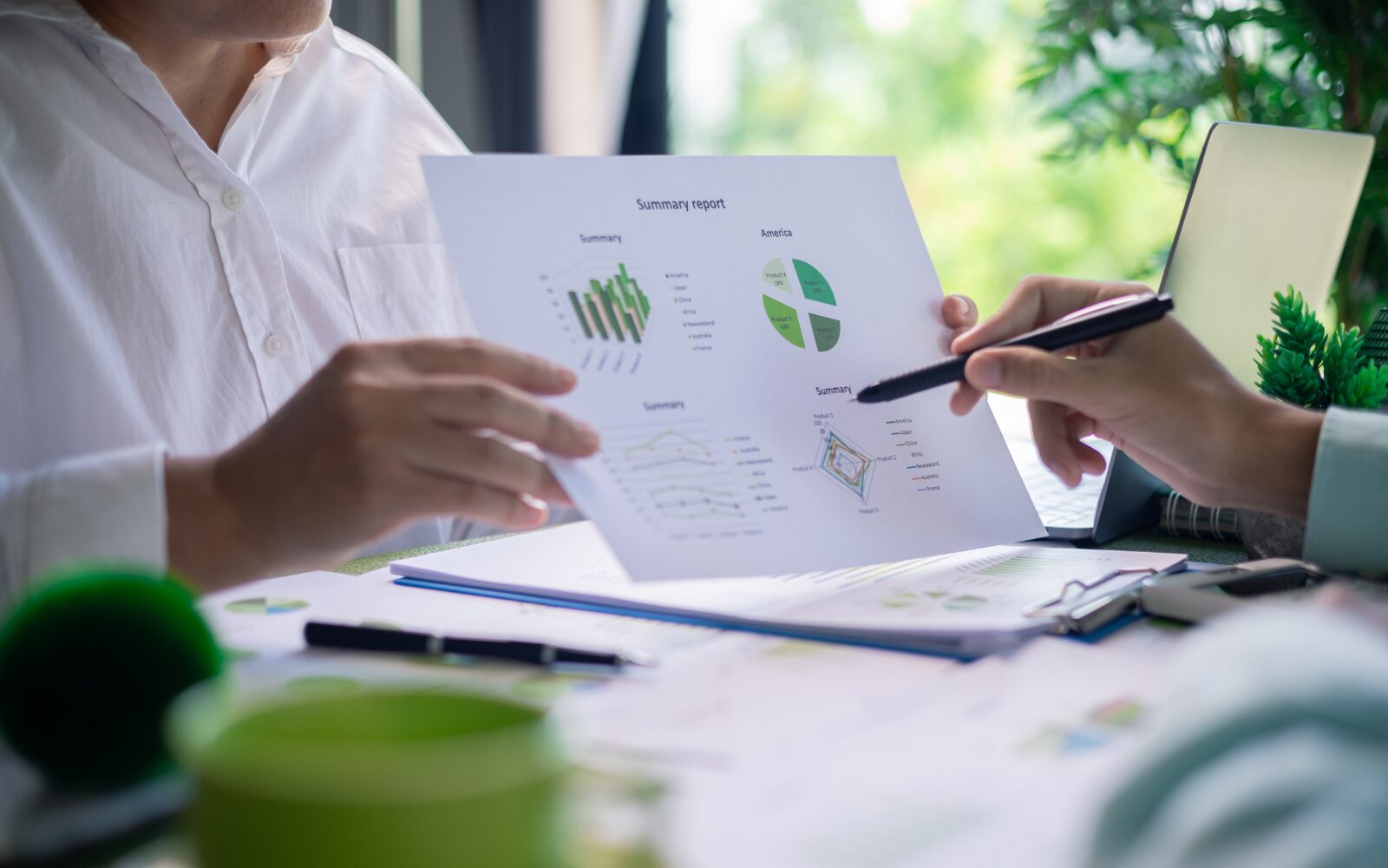 Two inclusion professionals reviewing their environmental sustainability policies. One person is holding up a sheet of paper with a green graph, the other is pointing to a piece of data on the sheet with their pen.