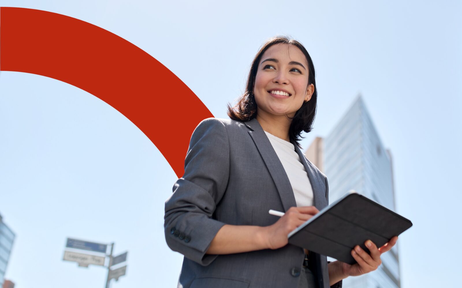 A photo of a women with a short brown bob haircut, dressed in a grey jacket and white t-shirt. She is looking off to the left of the photo. She is smiling and has a tablet in her hands.
