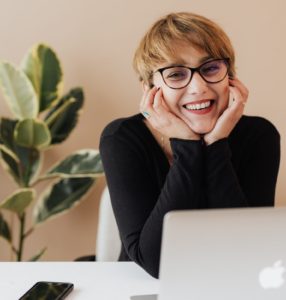 Woman working at a laptop. She is smiling and resting her head in her hands