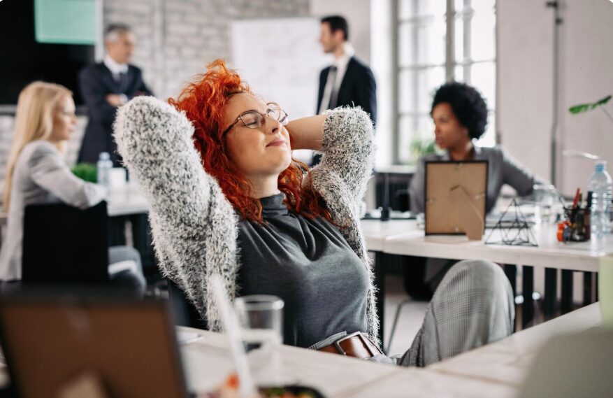 Young creative businesswoman with hands behind head taking a break and resting with eyes closed in the office