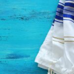 A white with blue and gold striped detailed Jewish pray shawl.